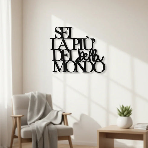 Black wooden wall art with Italian phrase 'Sei la più bella del mondo' in minimalist living room with armchair and plant