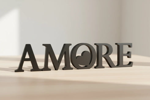 Black wooden decorative letters spelling AMORE placed on light wood surface in bright room