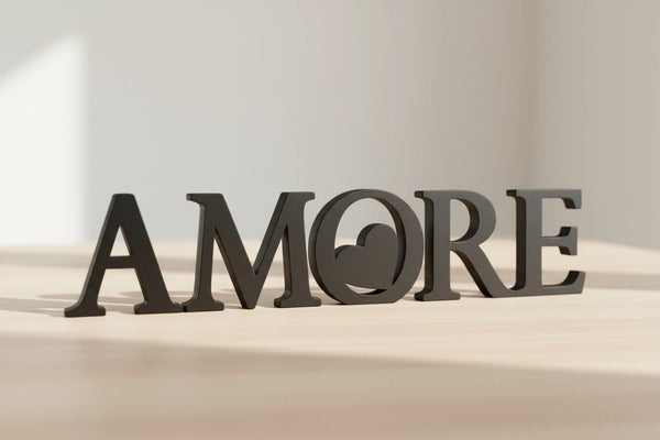 Black wooden decorative letters spelling AMORE placed on light wood surface in bright room