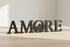 Black wooden decorative letters spelling AMORE placed on light wood surface in bright room