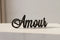 Black wooden decorative script word 'Amour' on a light surface, modern home decor