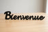 Black wooden Bienvenue sign on light wood surface for home decoration
