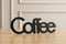 Black wooden decorative word 'Coffee' on wooden table with beige paneled wall background