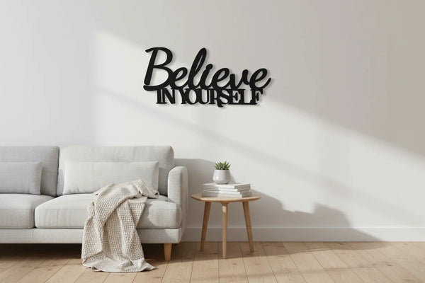 Modern living room with light gray sofa, wooden side table, and black wooden wall decor saying Believe In Yourself