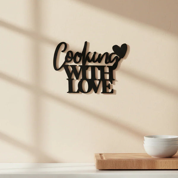 Black wooden wall decor sign saying Cooking With Love in kitchen with white bowls and wooden cutting board