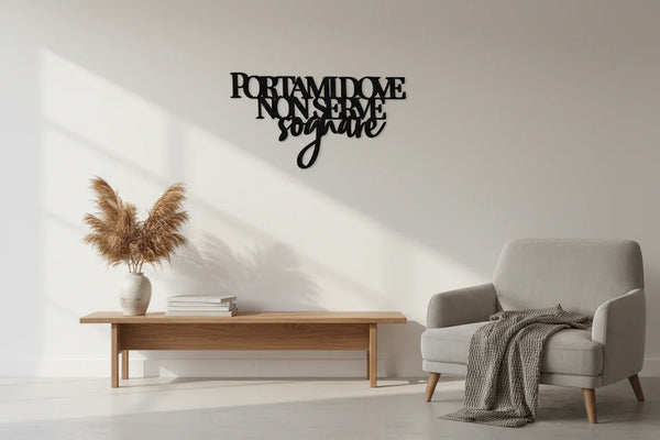Minimalist living room with wooden bench, white vase with pampas grass, gray armchair, and black wall art saying 'Portami dove non serve sognare'