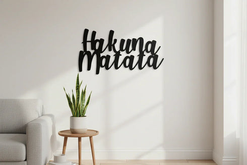 Modern living room with grey sofa, wooden side table, potted plant, and black wooden Hakuna Matata wall decor