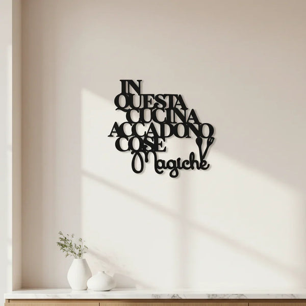 Black wooden kitchen wall decor saying in Italian "In questa cucina accadono cose magiche" on white wall with small vases on countertop