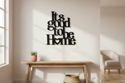 Minimalist home interior with black wooden wall art saying It's good to be Home, wooden table with plant, beige armchair