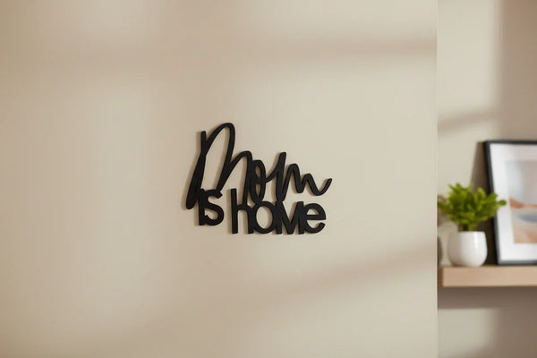 Black wooden wall decor sign reading 'Mom is Home' on beige wall in cozy home setting