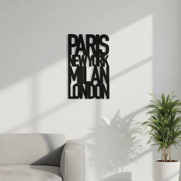 Minimalist living room with grey sofa, green plant, and black wooden wall decor featuring city names Paris, New York, Milan, London