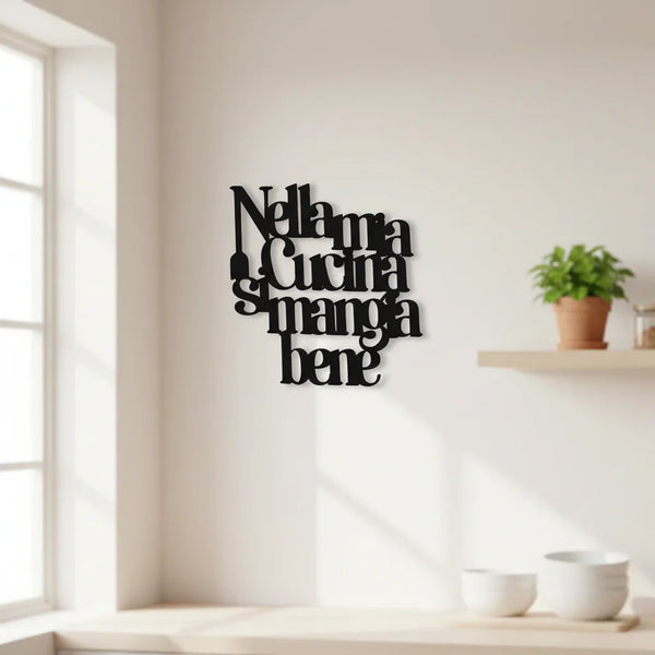 Black wooden kitchen wall decoration with Italian text 'Nella mia cucina si mangia bene' on white wall near window and plant