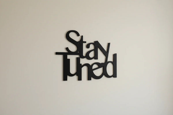 Black wooden wall decoration with the words 'Stay Tuned' on a light beige wall in home decor style