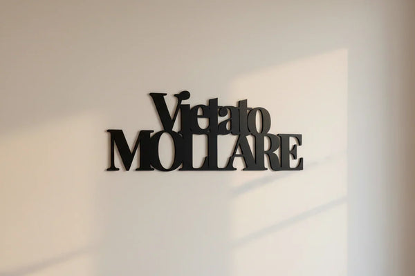 Black wooden wall decoration with Italian phrase 'Vietato Mollare' on light beige wall