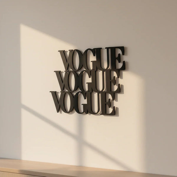 Black wooden wall decor with the word VOGUE repeated three times hung on beige wall with sunlight shadow