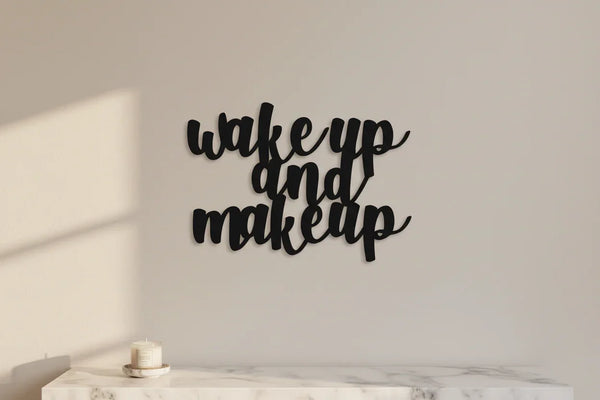 Black wooden wall decor with phrase 'wake up and make up' above a white marble surface and a small candle