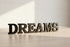 Black wooden block letters spelling 'DREAMS' on a light wood surface with soft natural lighting