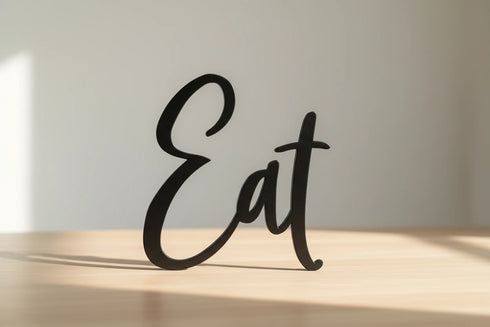 Black wooden decorative word 'Eat' standing on light wooden surface in bright natural light