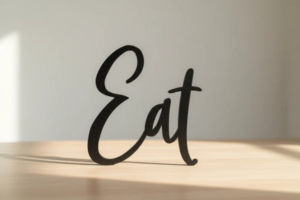 Black wooden decorative word 'Eat' standing on light wooden surface in bright natural light