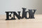 Black wooden decorative letters spelling ENJOY on a light wooden surface with neutral background