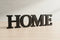 Black wooden letters spelling HOME on light wood surface, minimal home decoration
