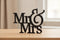Black wooden Mr & Mrs decorative sign on light wood table with blurred neutral background