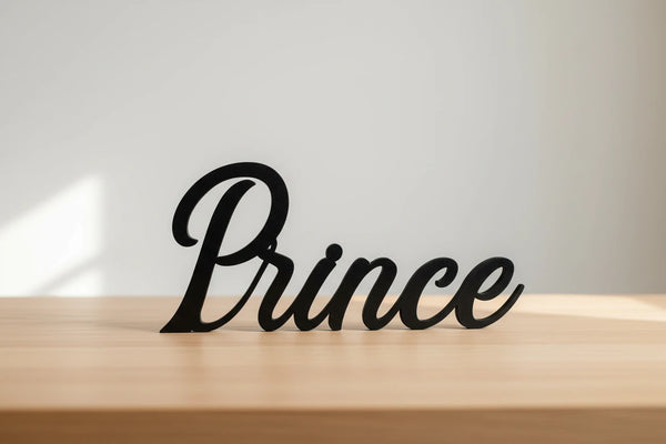 Black wooden decorative word 'Prince' displayed on a light wood surface against a plain white wall