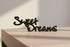 Black wooden 'Sweet Dreams' home decor sign on light wood surface with soft lighting